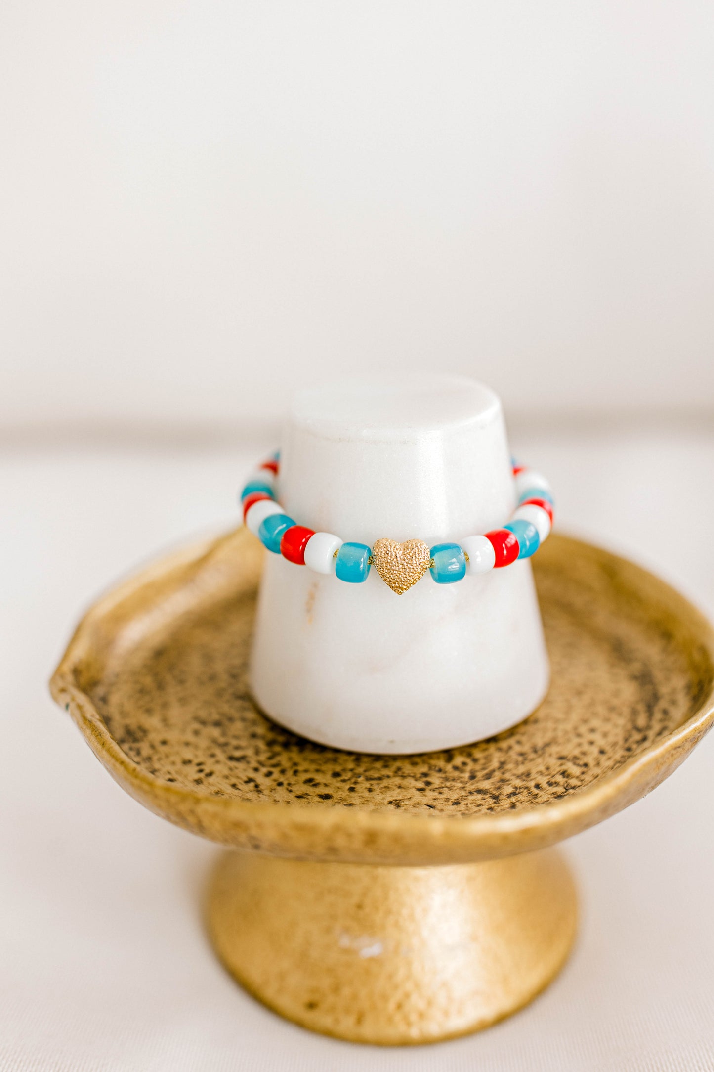 The perfect bracelet to show off your love for the red, white, and blue! Made with forte gemstone paired with an18k gold filled heart all strung using gold lurex cord.