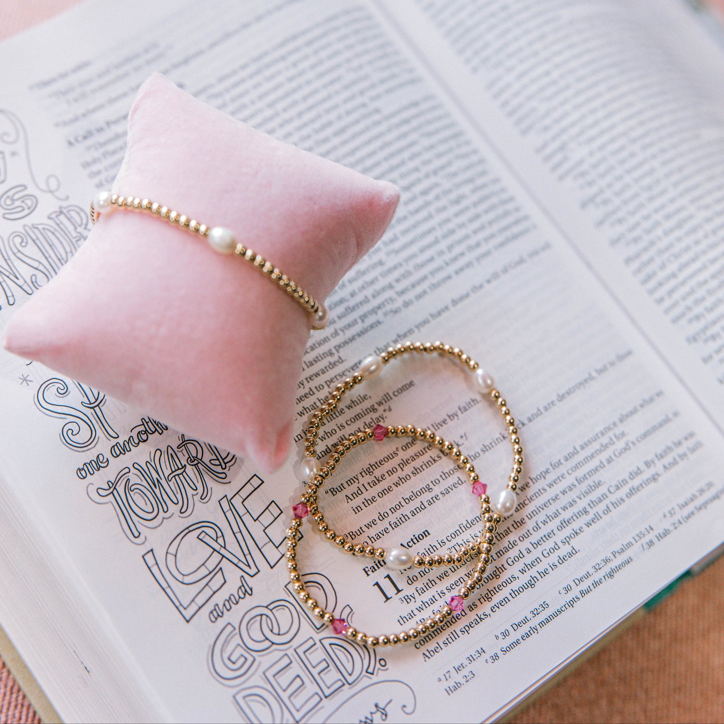 Gold bracelets on an open book with a pink pillow in the background