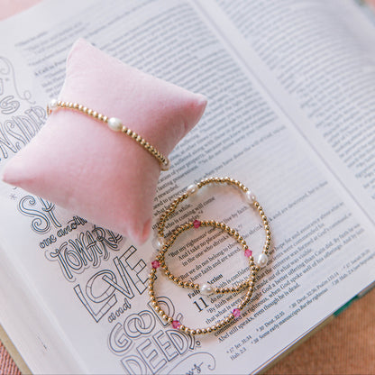 Gold bracelets on an open book with a pink pillow in the background