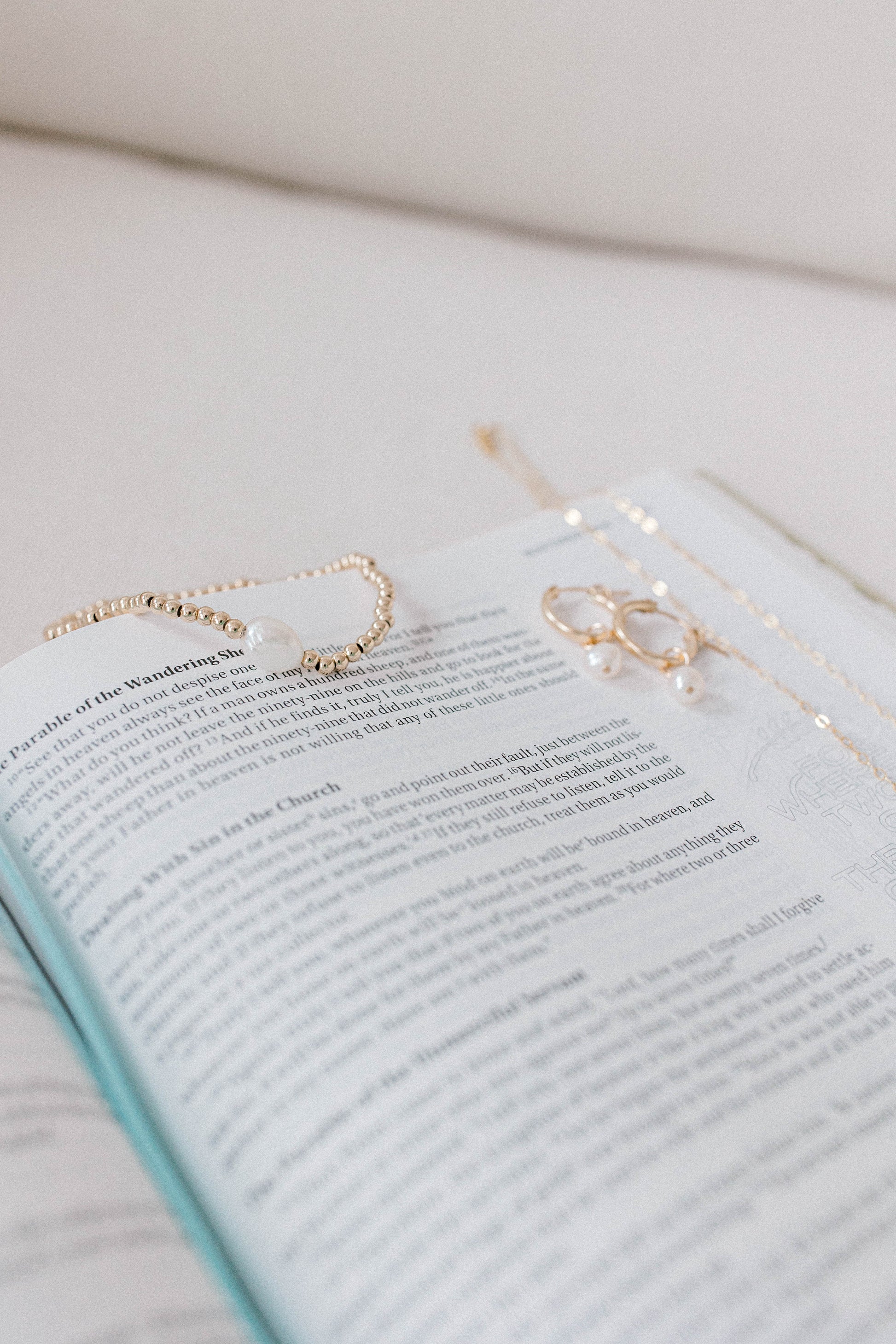 A photo of a bible with the He Left the 99 jewelry collection laying on top including a necklace, earrings, and bracelet. All gold with a single pearl.