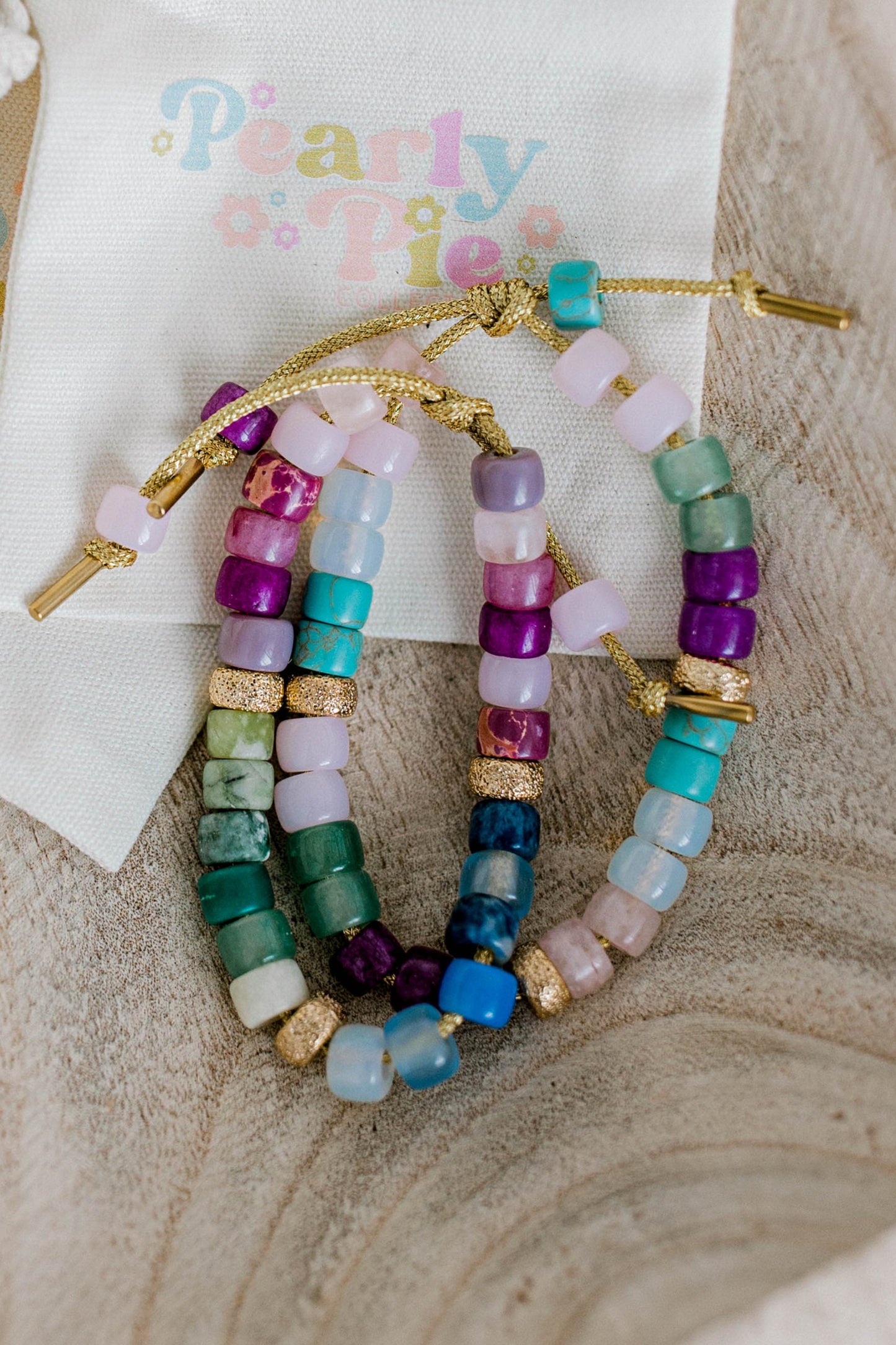 A beautiful handmade bracelet called the Moody Forte Bracelet. It is made with a variety of moody, yet beautiful, colored forte gemstones and 18k gold filled stardust spacer beads that are strung on lurex cord with an adjustable sliding knot including a beautiful heart bead as a finishing touch. It can also be made with or without the heart bead.