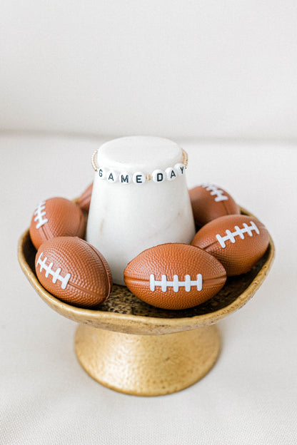 14k gold beaded game day bracelet with white letter beads posed on a cute football themed display. Handmade using the highest quality materials.