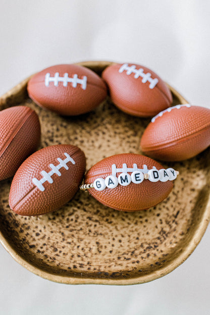 14k gold beaded game day bracelet with white letter beads posed on a cute football themed display. Handmade using the highest quality materials.